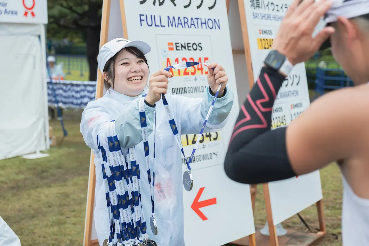 横浜マラソンのランナーに笑顔で完走メダルを渡すボランティア